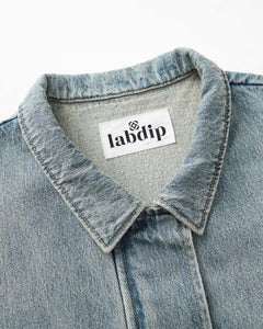 Détail du col d’une veste en denim bleu délavé avec couture apparente, tissu en coton robuste et étiquette de la marque Labdip.