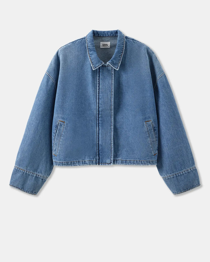 Veste en denim bleu clair en coton, coupe droite et courte avec col classique, manches longues légèrement larges et poches latérales discrètes.