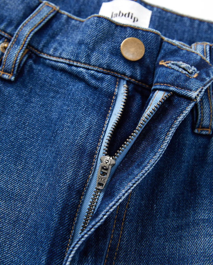 Jean large en denim bleu 100 % coton avec fermeture éclair métallique, coupe mi-haute et coutures contrastantes, idéal pour femme recherchant confort et style adaptable.