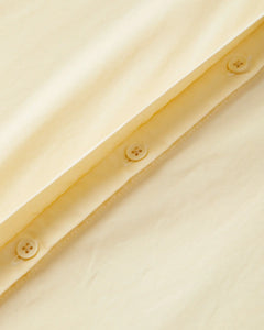 Détail en gros plan d'un tissu popeline vanille doux avec boutons, montrant la texture légère et la qualité du matériau idéal pour un pantalon d'été féminin.