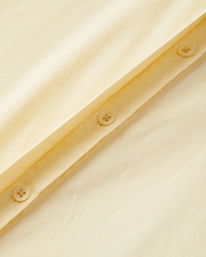 Détail en gros plan d'un tissu popeline vanille doux avec boutons, montrant la texture légère et la qualité du matériau idéal pour un pantalon d'été féminin.