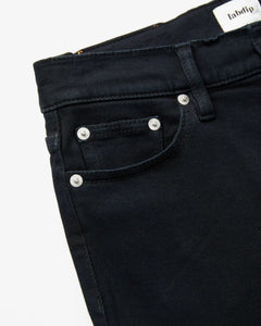 Jean femme en denim noir profond, coupe droite et ajustée, matière 100% coton, avec rivets métalliques et poche avant discrète pour un style élégant et confortable.