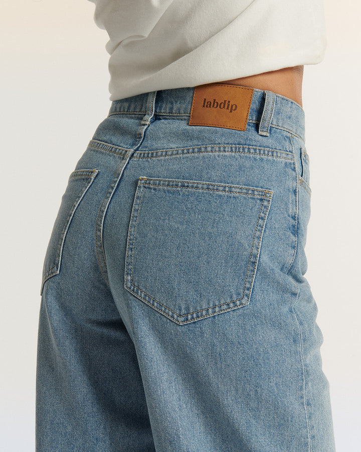 Jean en denim 100 % coton de couleur bleu clair, coupe droite et taille mi-haute, avec une texture légèrement rigide et une poche arrière simple.
Jean ballon JEMMA en denim bleu clair porté par le mannequin, détail de dos et des poches, coloris IN 27.