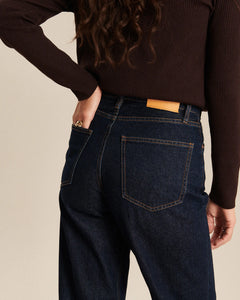 Jean droit en denim brut bleu foncé 100 % coton, coupe large et confortable, avec coutures marron apparentes et poche arrière classique, idéal pour femme.