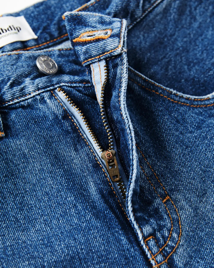 Jean en denim bleu moyen 100 % coton avec fermeture éclair, coupe droite et ajustée, coutures orange apparentes, idéal pour femme.