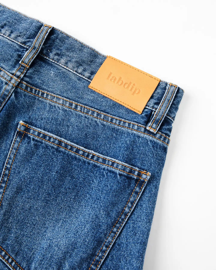 Jean femme en denim bleu moyen, 100 % coton, coupe droite et ajustée avec étiquette en cuir beige, offrant un maintien confortable et un style intemporel.