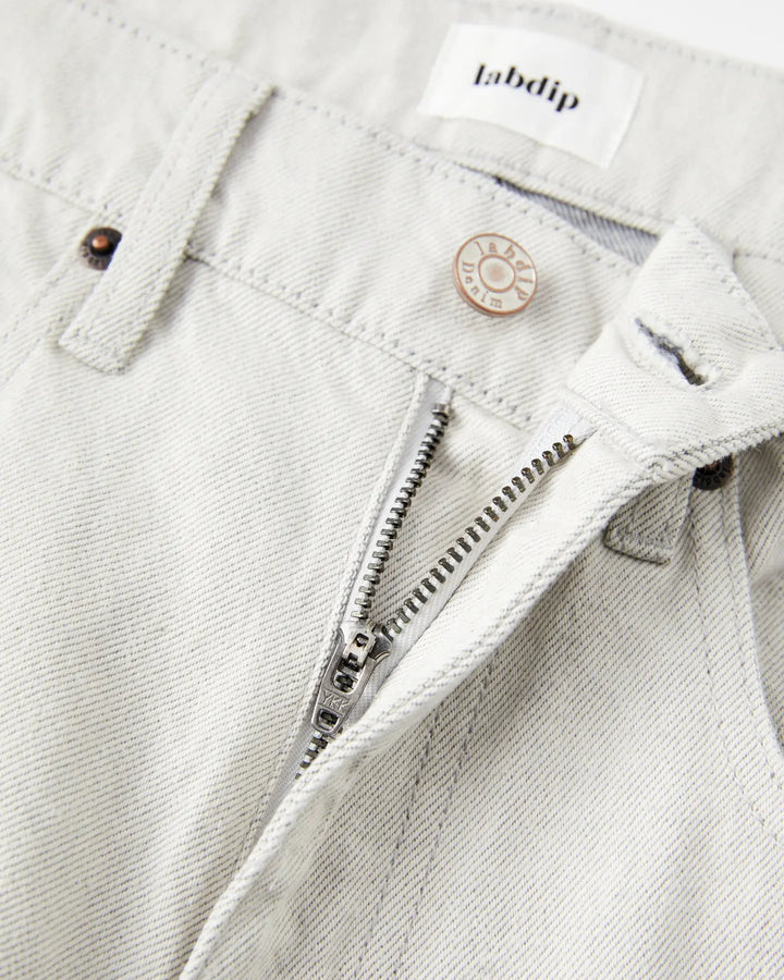 Jean pour femme en denim non teinté couleur granit clair, coupe droite avec fermeture éclair et bouton métal gravé, confection 100% coton avec finition sobre et naturelle.