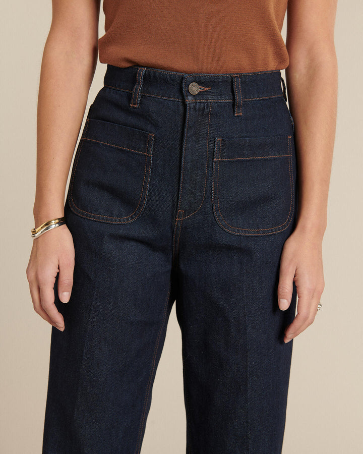Jean femme en denim brut bleu foncé, coupe droite légèrement ample avec poches plaquées frontales et couture contrastée, en coton robuste et confortable.